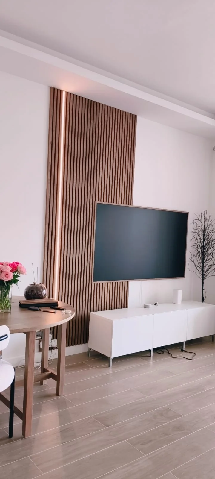 Living-room wall with a tall slatted acoustic panel, an LED strip along its edge and a wall-mounted television
