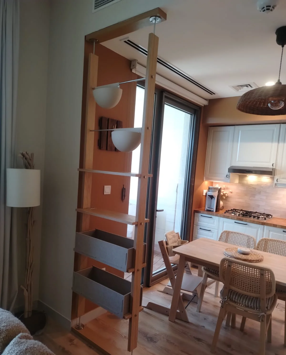 Floor-to-ceiling room divider with two bowl lights, shelves and two boxes, fixed between floor and ceiling next to a kitchen and dining table