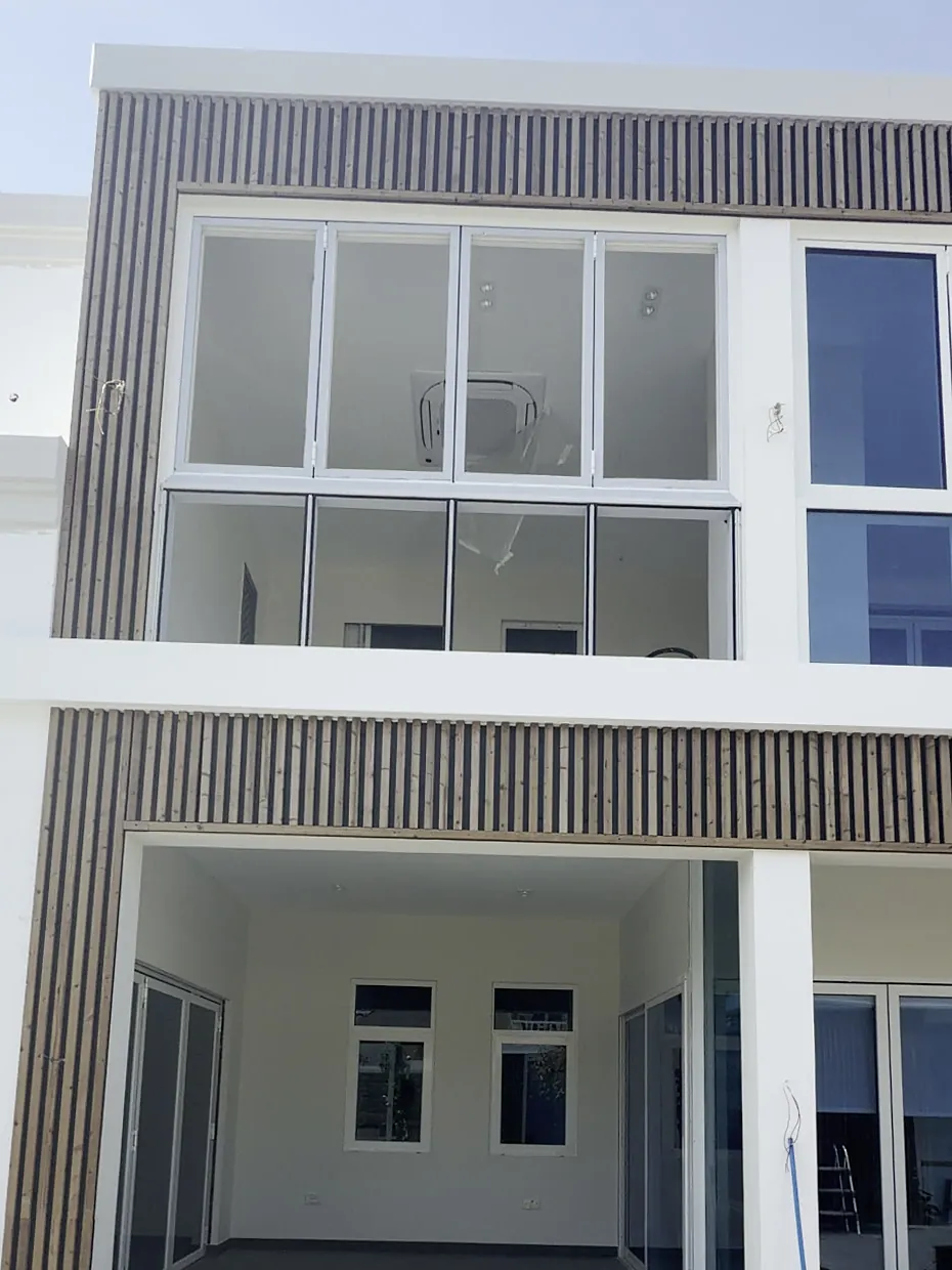 Two-storey villa façade with dark slatted Aluwood cladding framing the upper glazing and the covered terrace below